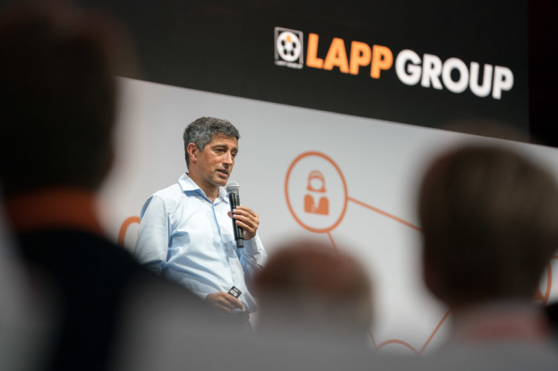 Event photography, editorial photography: The science journalist Ranga Yogeshwar gives a lecture at a Lapp Kabel event for guests, company employees and their families. In the background you can see the logo of the company.