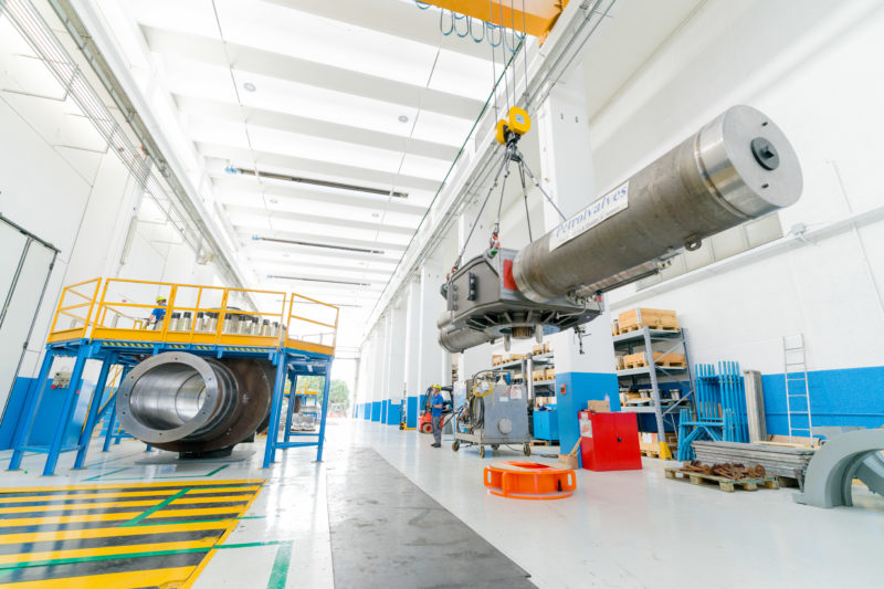 Industriefotografie: Der Regelkopf mit zwei hydraulisch angetriebenen Steuerungszylindern wird auf das links im Bild sichtbare Ventil einer Gaspipeline gehoben. An der Unterseite sieht man das große Zahnrad, das die Ventilstellkugel im Ventil antreiben wird.