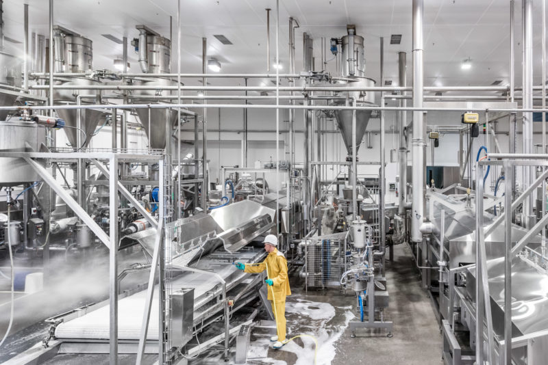 Industrial photography: Nightly high-pressure cleaning of a production plant for pastrys. One employee sprays all surfaces with a special disinfectant foam. The photo shows the complicated production line, built almost exclusively of stainless steel.