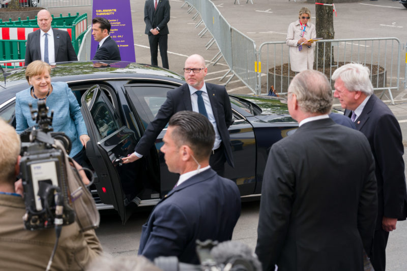 Reportagefotografie: Die Bundeskanzlerin Angela Merkel verlässt ihre Limousine um am Festakt eines Firmenjubiläums teilzunehmen. Sicherheitsleute, Gastgeber und der Ministerpräsident des Landes Hessen Volker Bouffier stehen zur Begrüßung bereit.