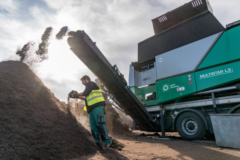 Reportage photography: An employee checks the quality of the soil sifted by a screening machine for compost waste.