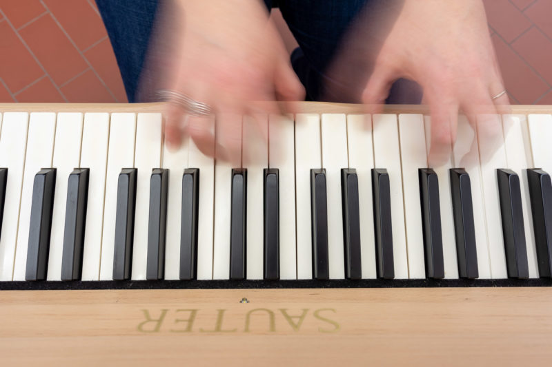 Reportage photography: Scientists create artificial ivory: Photo of a piano keyboard from above with artificial ivory and the moving hands of a player.