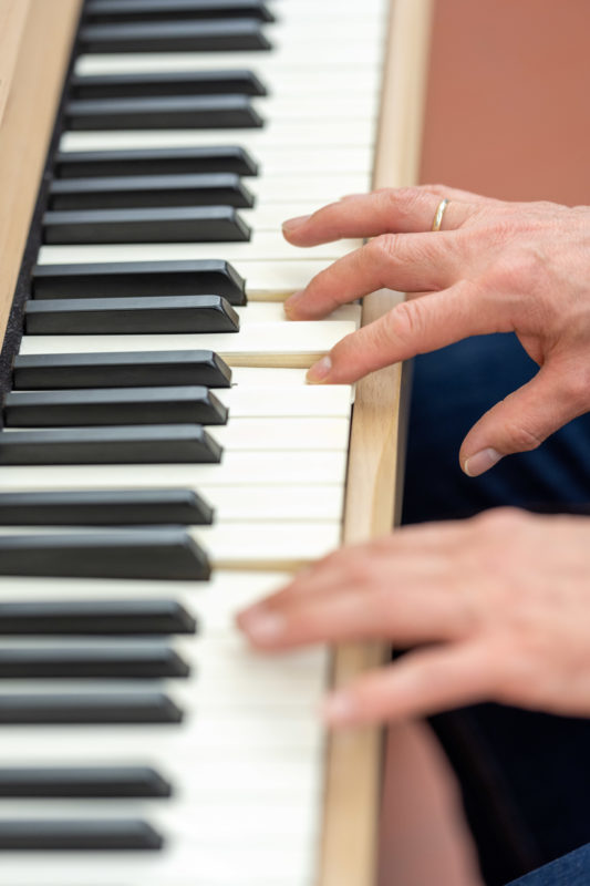 Reportage photography: Scientists create artificial ivory: portrait format of the keyboard with white keys made of the new material. You can see the hand of the player.