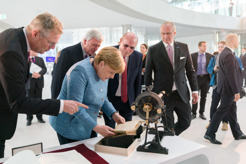 editorial photography: German Chancellor Angela Merkel at the celebration of the 350th anniversary of Merck in Darmstadt. She is looking at a book and other exhibits about the company