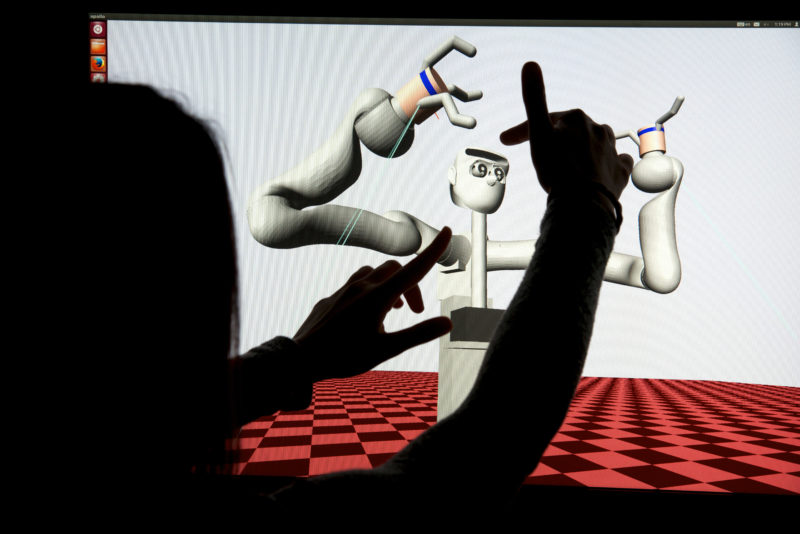Wissenschaftsfotografie: Simulation eines Roboters mit menschenähnlichen Gliedmaßen am Max-Planck-Institut für Intelligente Systeme. Man sieht auf dem Bildschirm den vereinfacht dargestellten Roboter und seine Bewegung, während eine Wissenschaftlerin mit ihren fingern die Bewegungsradien andeutet.