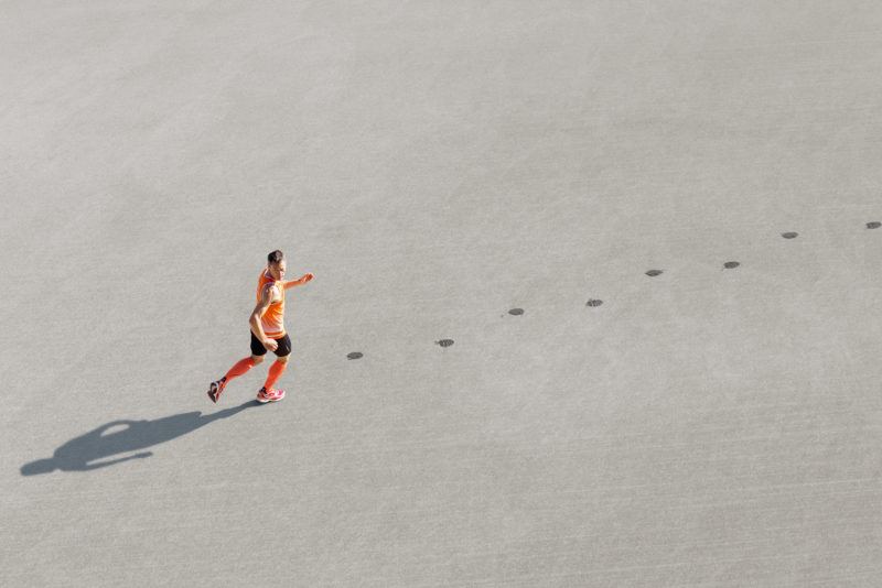 Photomontage with Photoshop: A reverse running athlete runs over the asphalt and leaves wet footprints.