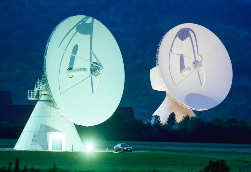 Industriefotografie: 2 große Satelliten-Empfangsantennen bei Nacht in einer Bodenstation.