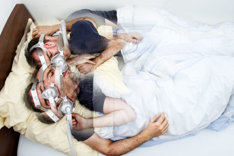 Photomontage with Photoshop: A man wallows in bed at night in a sleep laboratory. He has a mask on his face.