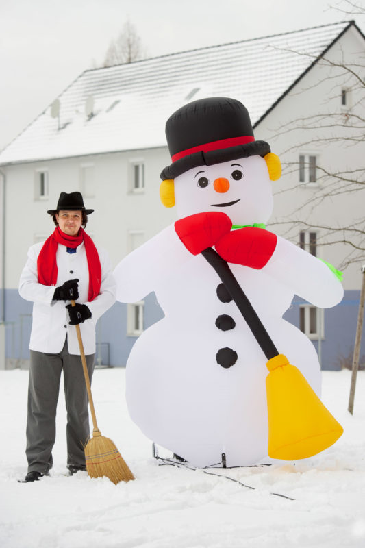 Mitarbeiterfotografie: Als Hobby sammelt dieser Mann Schneemänner aus aller Welt. Hier steht er in derselben Pose und Kleidung neben der größten Figur in der Sammlung im Schnee.