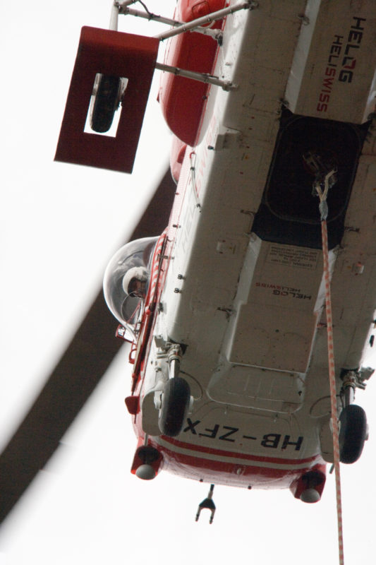 Technikfotografie: Ein russischer Kamov Ka-32 Schwerlasthelikopter einer Schweizer Spezialfirma wird zum Austausch einer Sendeantenne eingesetzt. Der Pilot kann durch ein spezielles Fenster beinahe senkrecht nach unten schauen, um die Last zu beobachten.