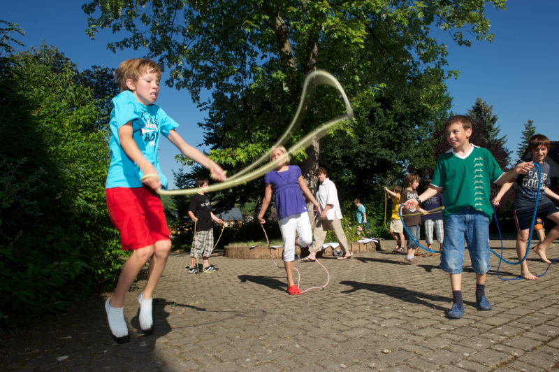 Editorial photography: Primary school children volunteer for sports during the break. Several of them do rope-hopping together in the schoolyard. The weather is fine and the sun is shining. Everybody