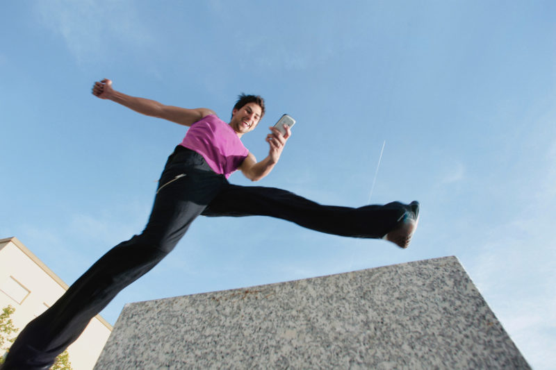 Special perspective from the floor: A young man makes a big jump while looking at his smartphone.