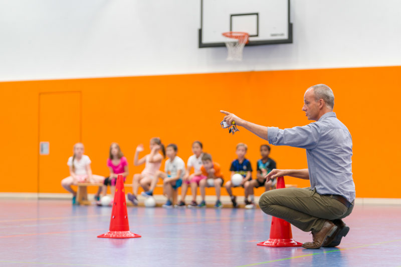 Editorial photography, subject learning and education: A sports teacher divides the teams for a ball game during lessons in a school sports hall. In his hand he has his whistle and the school keys.