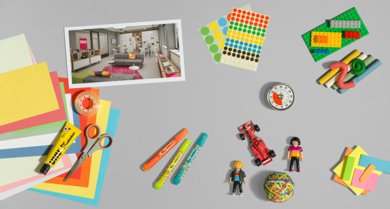 Studiofotografie: Table-Top-Aufnahme eines mit diversen bunten Spielzeugen und anderen Kleinteilen bestückten Tisches. Das Foto ist ein Symbol für kreatives Arbeiten nach der Design-Thinking Technik.