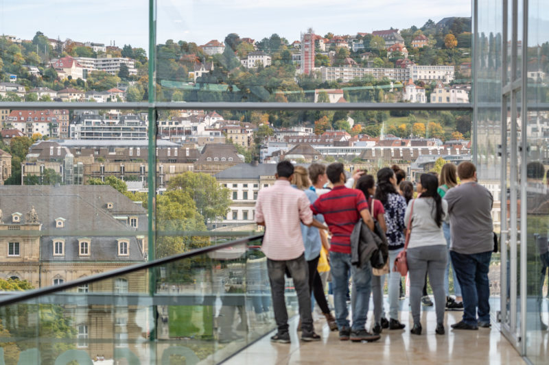 Stadtportrait Stuttgart: Eine Gruppe von Touristen besucht den obersten Stock des Kunstmueums Stuttgart und genießen den Blick auf die umliegenden bebauten Hänge.