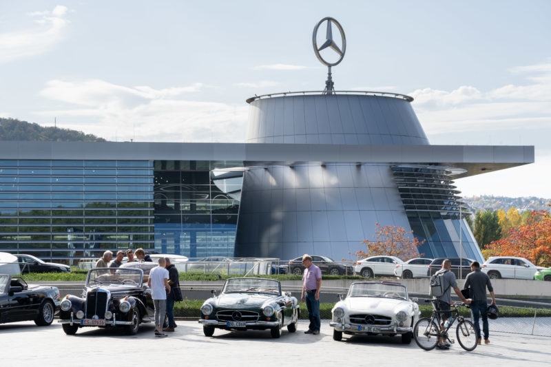 Stadtportrait Stuttgart: Auf dem Vorplatz des Mercedes-Benz-Museums stehen eine Reihe historische Mercedes Cabrios. Die Szene wird von einem großen Mercedes Stern auf dem Dach der angrenzenden Mercedes Niederlassung überragt.