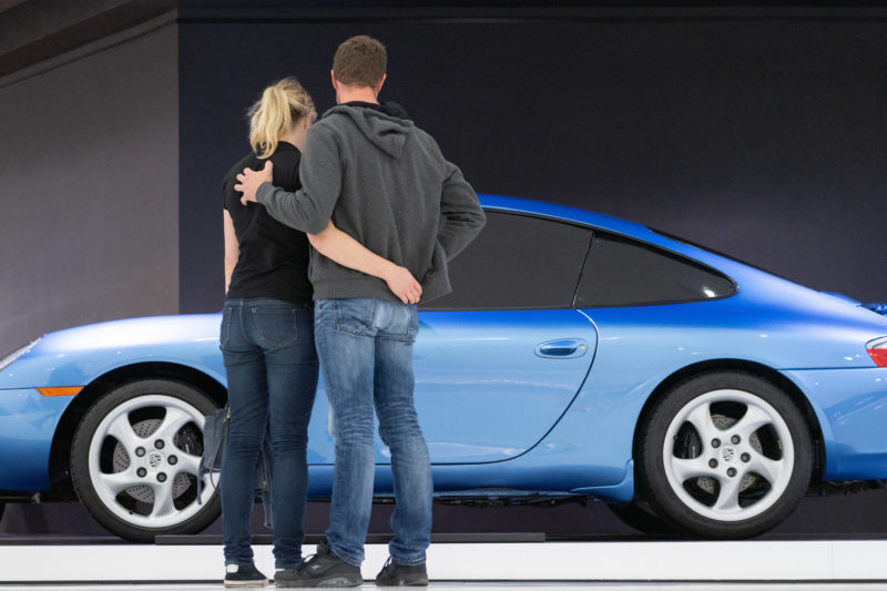 Stadtportrait Stuttgart: Im Porsche-Museum sieht man auch die modernsten Versionen der Porsche Sportwagen. Ein Paar steht umschlungen vor einem blauen Modell 911.