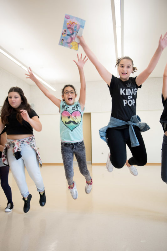 Editorial photography, subject learning and education: Girls jump into the air screaming and cheering during lessons in a theatre pedagogy workshop.