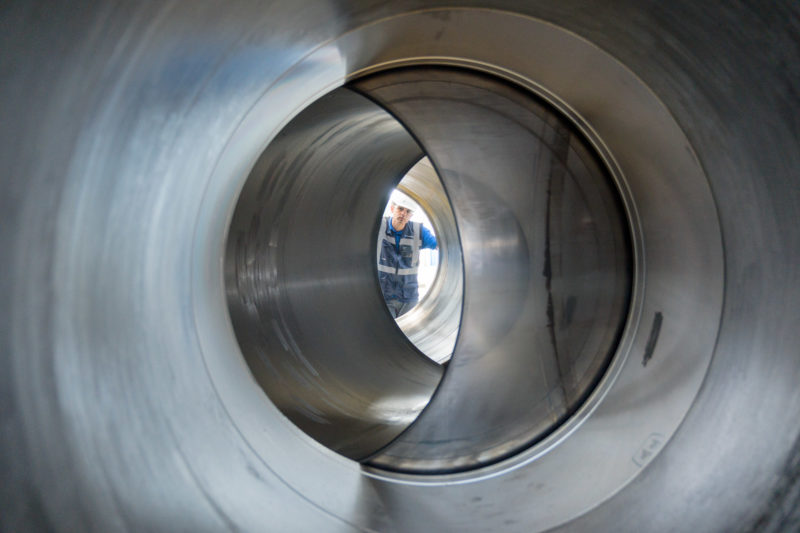 Industrial photography: An employee looks through the huge valve that will later be installed in a gas pipeline. The spherical closure element regulates the flow by rotating it in the valve.