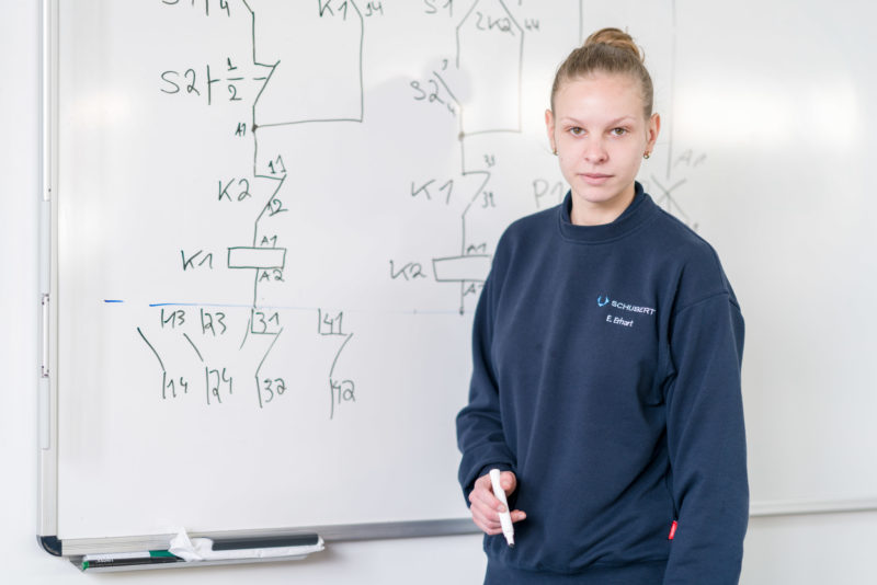 Editorial photography: A female trainee stands self-confidently on a white board in her company