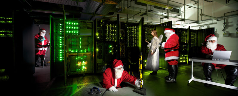 Photomontage with Photoshop: Christmas photo for an IT company: Red Santa Clauses and an angel work in the green-lit server room.