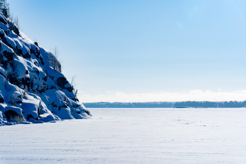 Landscape photography: Winter in Finland: View of an ice-covered Baltic Sea bay, on the left typical rocks at the Baltic coast of Finland.