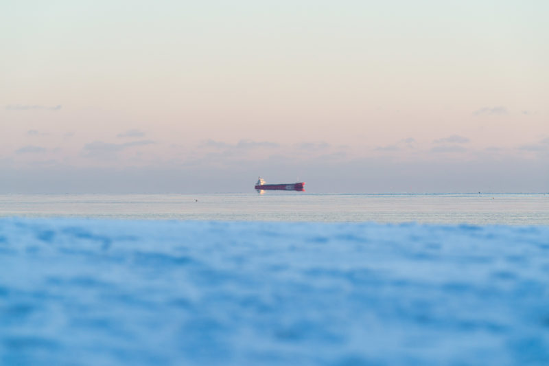 Landschaftsfotografie: Winter in Finnland: Ein Schiff fährt am Horizont im Wasser der eiskalten winterlichen Ostsee. Durch die Luftbewegungen und Spiegelungen sieht es aus, als würde es in der Luft schweben.