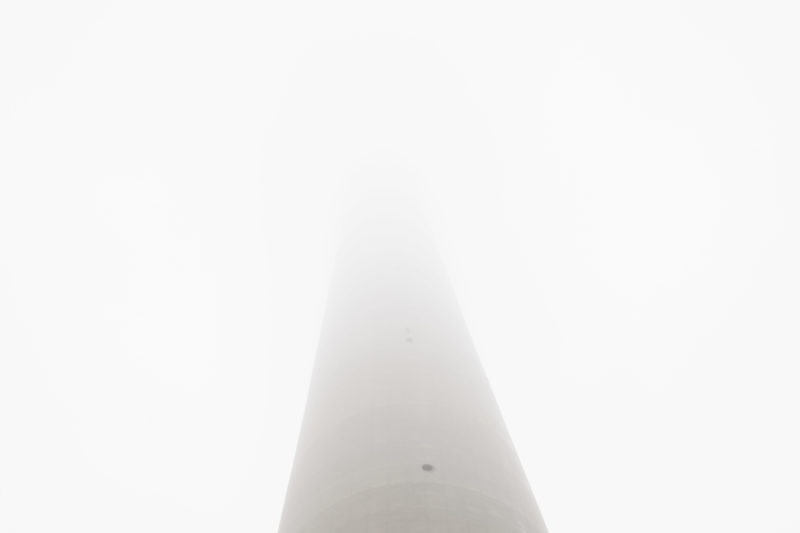 Der Frankfurter Europaturm im Nebel. Unten sieht man den grauen, langen Schaft aus Beton, wie er ab der Mitte des Bildes im weißen Nichts verschwindet.