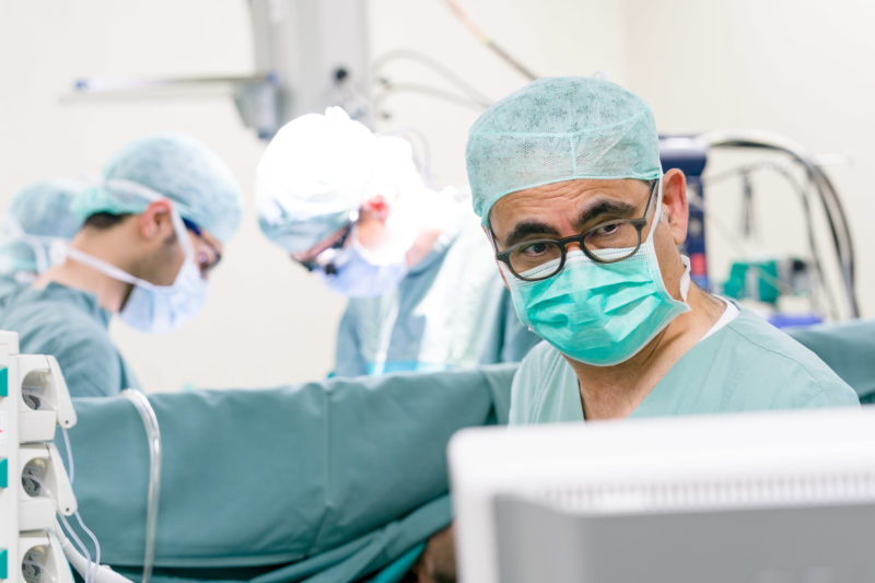 Healthcare photography:  An experienced heart surgeon before an operation begins. He checks the existing images and data on a display next to the operating table.