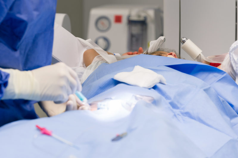 Healthcare photography: A girl is lying on the examination table in the cardiac catheter lab. You can see his long eyelashes behind the sterile surgical field.