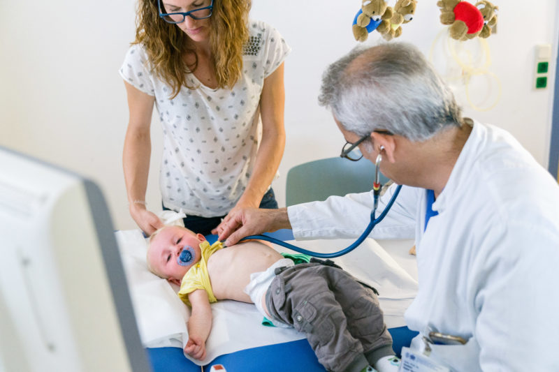 Medizinfotografie: In der kinderkardiologischen Abteilung der Universitätsklinik Homburg (Saar) wird während der Sprechstunde ein kleiner Junge untersucht. Seine Mutter betreut ihn am Untersuchungstisch, während der Arzt mit einem Stethoskop die Herztöne abhört.