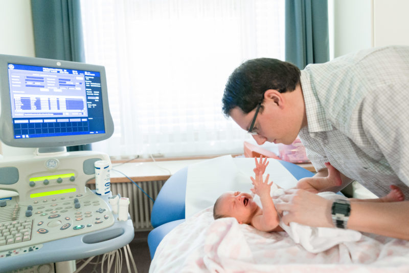 Healthcare photography:  In the pediatric cardiology department, a father takes care of his crying baby.